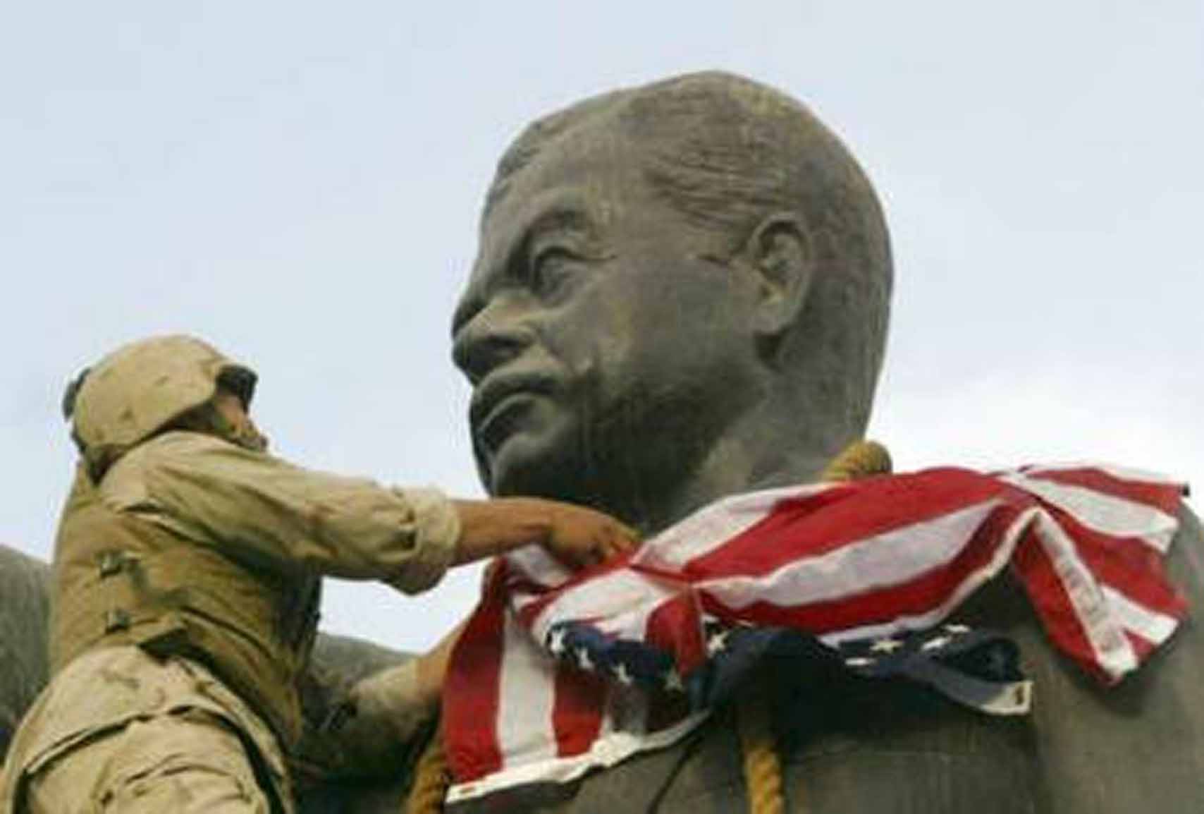 A United States Marine places an American flag over a statue of Saddam Hussein in Baghdad in 2003